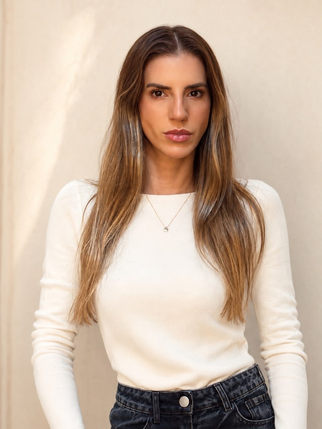 Retrato da Fafá de blusa off-white e jeans escuro, olhando para a câmera, diante de uma parede clara